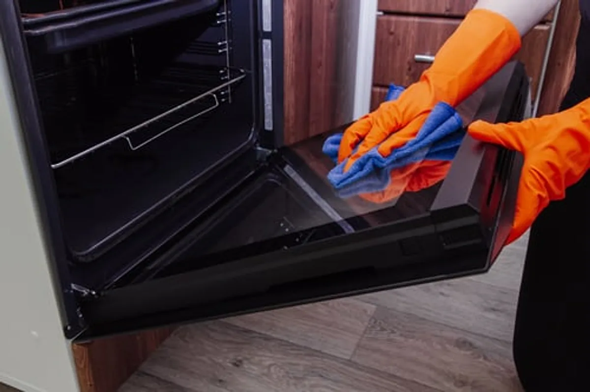 Cleaner in protective gloves degreasing an oven interior during a deep clean