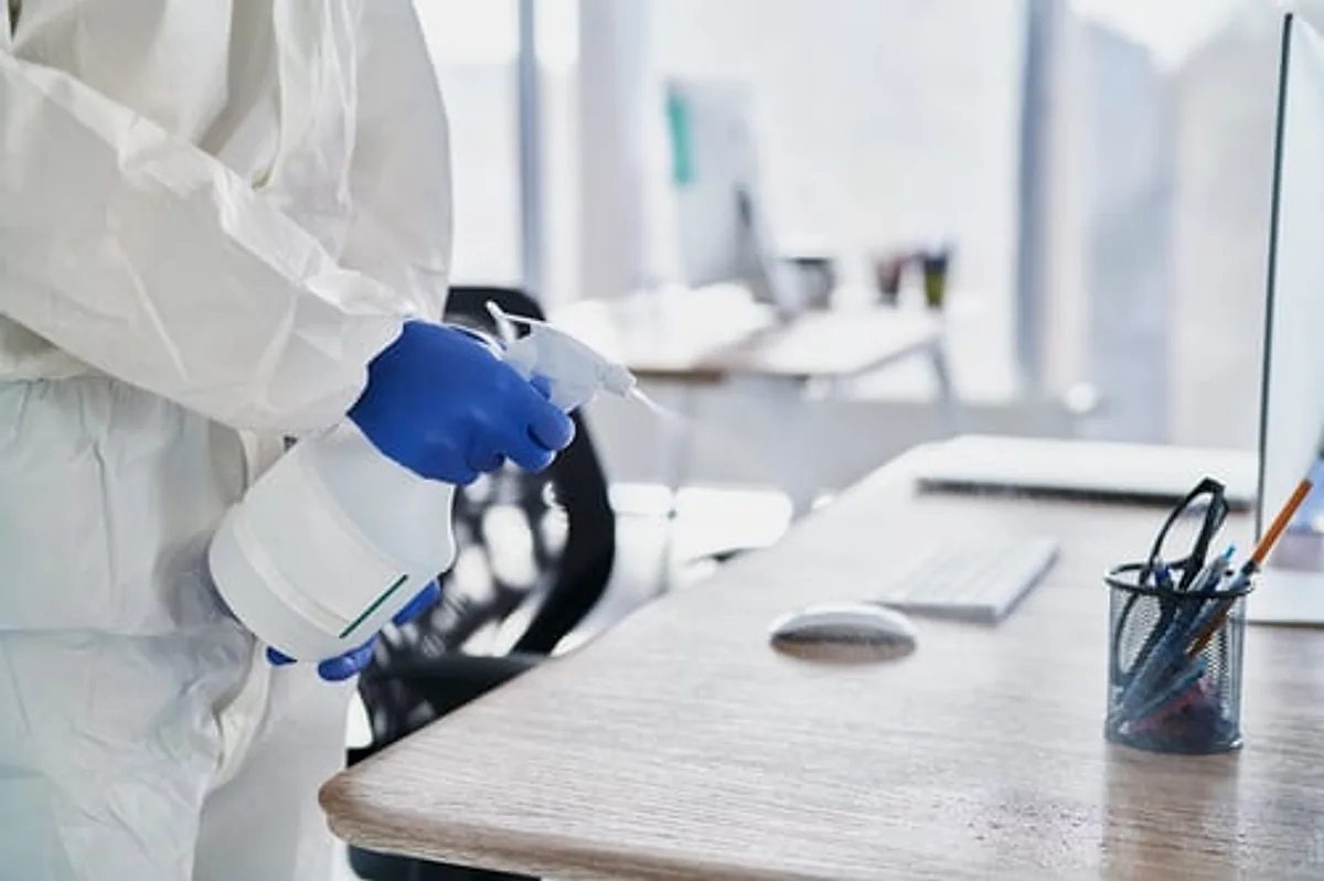 Cleaning technician in protective gear disinfecting an office desk and workstation