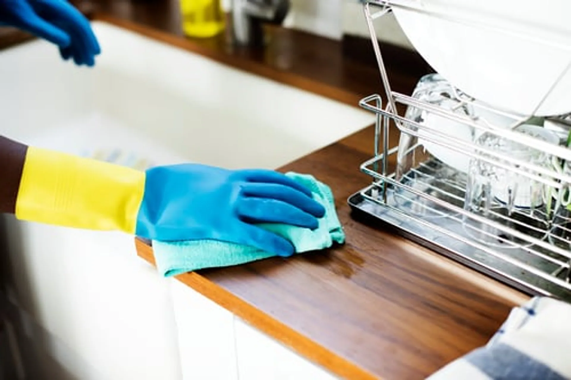Cleaner wiping down a kitchen counter beside a dish rack