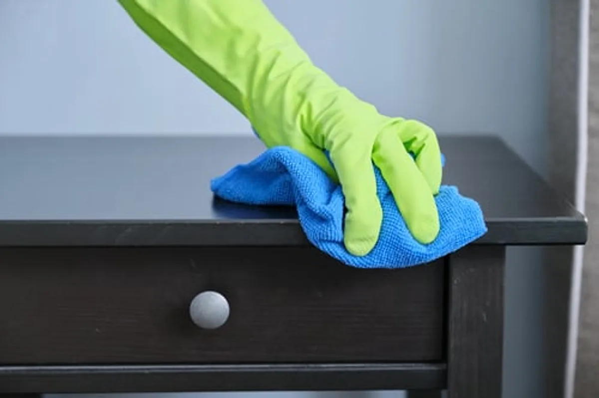 Gloved cleaner wiping down a dark wood surface during residential cleaning