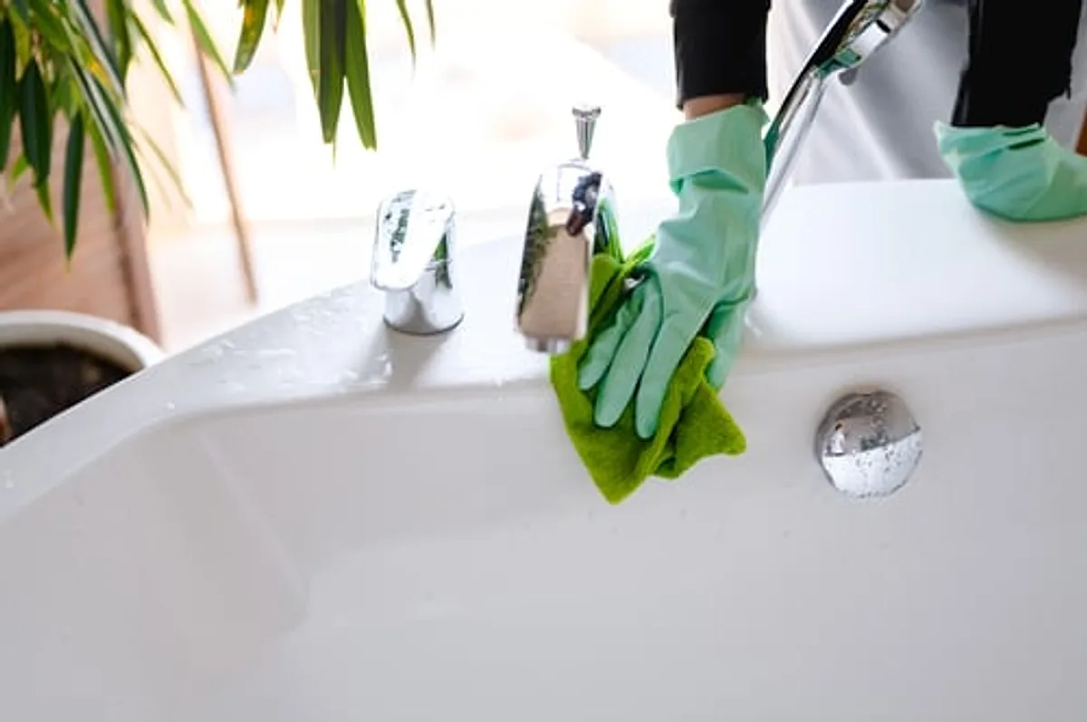 Cleaner wiping a bathroom sink and fixtures during a standard cleaning visit